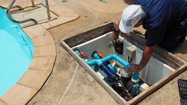 Technician working on pool circulation equipment beside a swimming pool